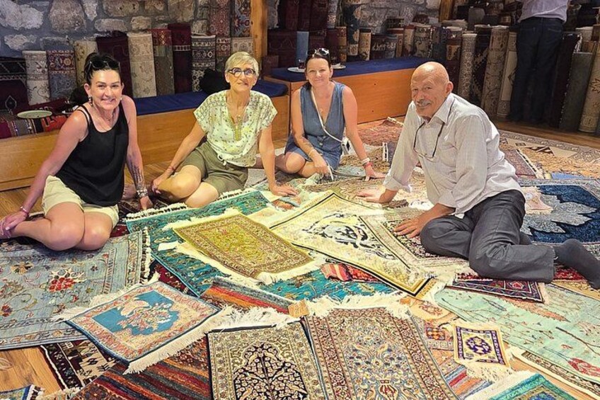 Four people sitting on the floor surrounded by various rugs. 3