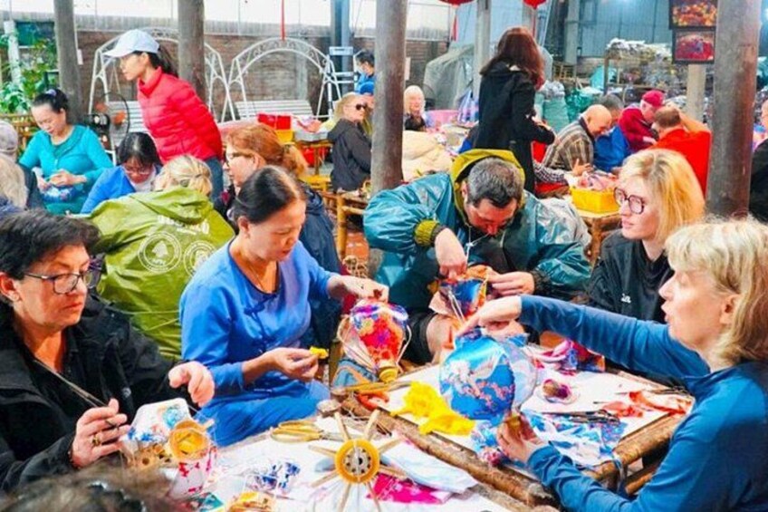 Folk er i gang med en håndgørelse, måske maleri eller pyntning, med forskellige redskaber og materialer på et bord. 5