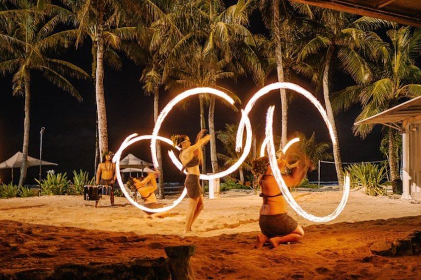 Une scène nocturne sur une plage, avec des personnes pratiquant la danse avec le feu, des palmiers et une plage de sable. 3