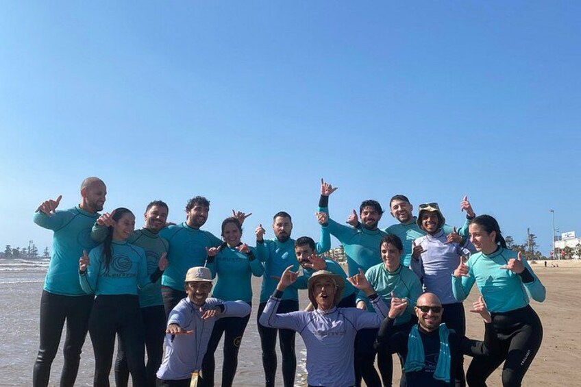 A group of people on a beach, some wearing wetsuits, with a clear sky and ocean in the background. 5