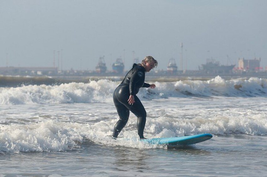 A person surfing on a blue board in the ocean with industrial structures in the background. 4