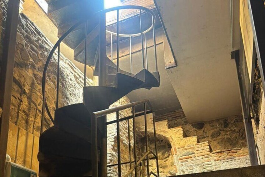 A spiral staircase in a stone-walled room with a metal railing. 3