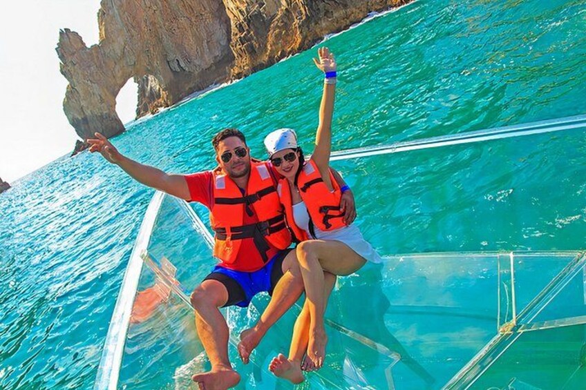 A couple on a boat with clear blue water and a rocky coastline. 1