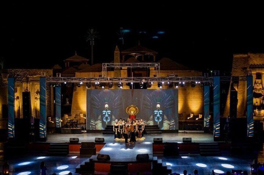 A stage with a large screen displaying a figure, surrounded by a crowd. 3