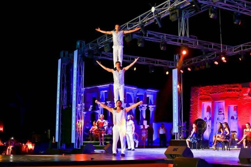 A circus performance with acrobats on a stage with a backdrop of classical architecture. 1