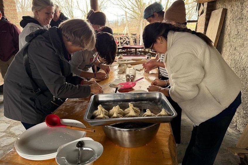 A group of people preparing food, with a focus on dumplings and a metal container on the table. 1
