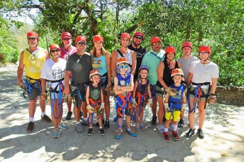 A group of people in helmets and life vests, standing on a paved path with trees in the background. 2