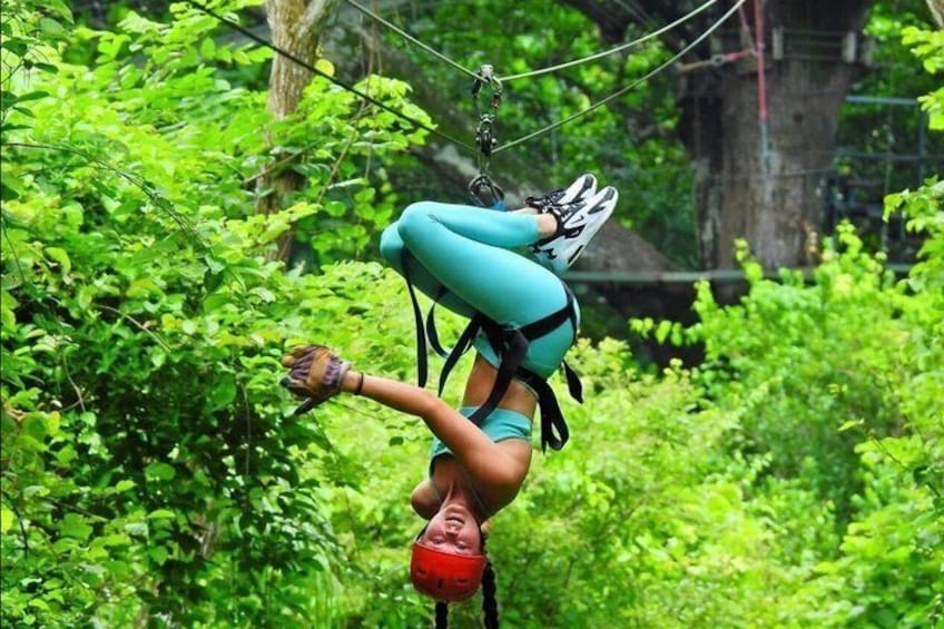 A person performing an acrobatic handstand on a zip line in a forested area. 5