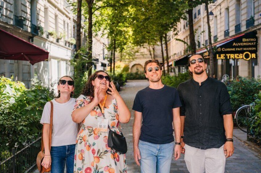 A group of people walking on a tree-lined street with buildings and a restaurant in the background. 1