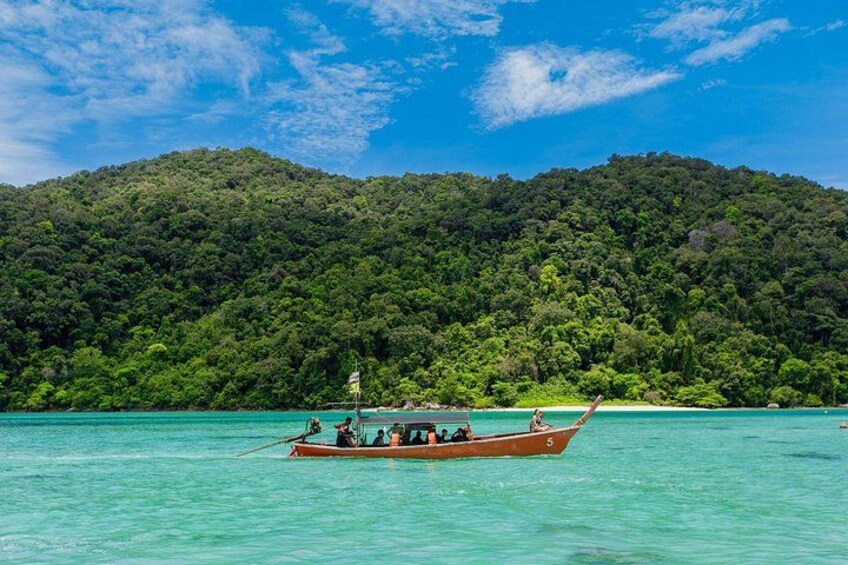 A boat on turquoise water with a forested island in the background. 3