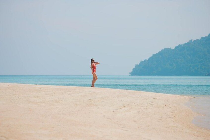 A beach with a person in a swimsuit standing on the sand, a clear sky, and a distant hill. 4