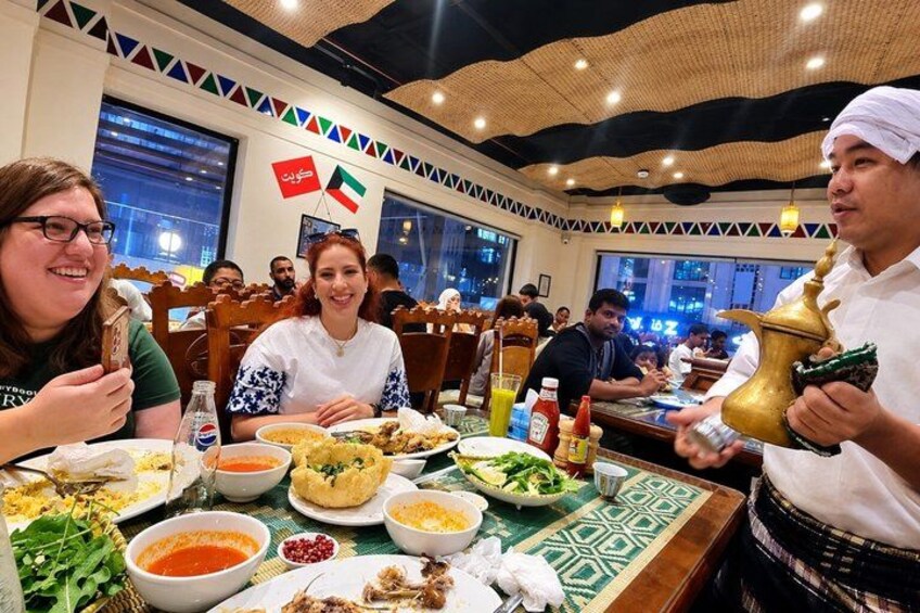 A restaurant with tables set for dining, various dishes, condiments, and a person holding a traditional brass water vessel. 2