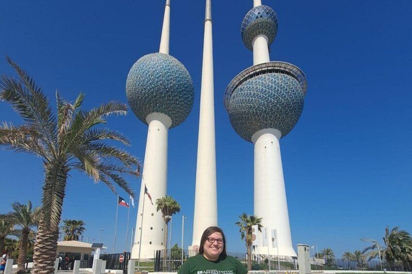 A person standing in front of three tall towers with spherical tops, palm trees, and flags. 1