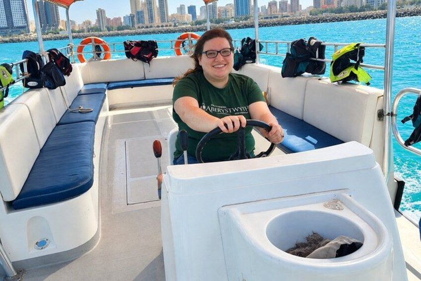 A person steering a boat with life jackets and a city skyline in the background. 3