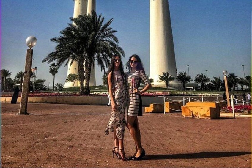 Two people posing in front of a lighthouse with palm trees and flowers in the background. 4