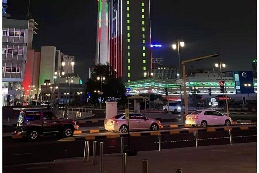 A nighttime cityscape with illuminated buildings, a busy intersection, and a prominent tower with vertical lights. 3