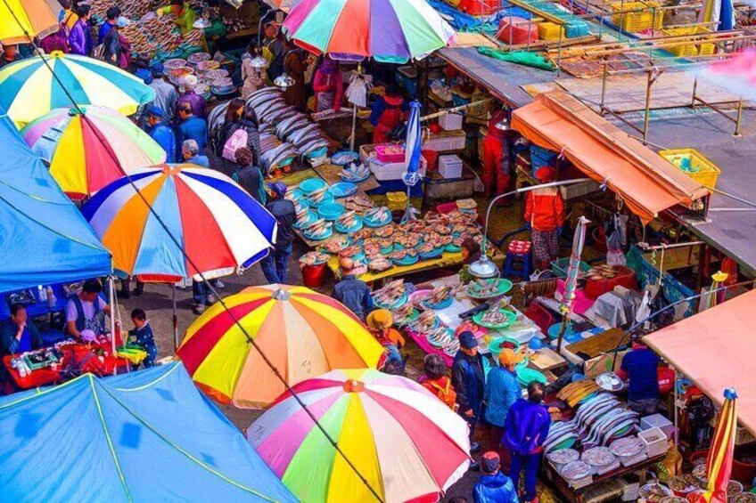 Un mercado al aire libre concurrido, con sombrillas de colores y diversos puestos que ofrecen productos. 5