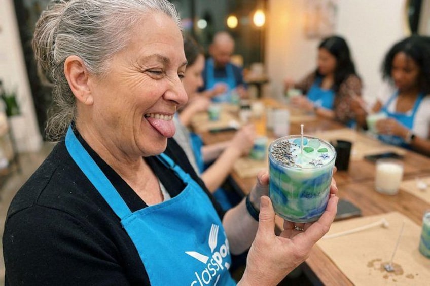 Una persona sostiene una bebida colorida con pajita, usando un delantal azul con un logo, en un ambiente interior informal con otras personas al fondo. 3