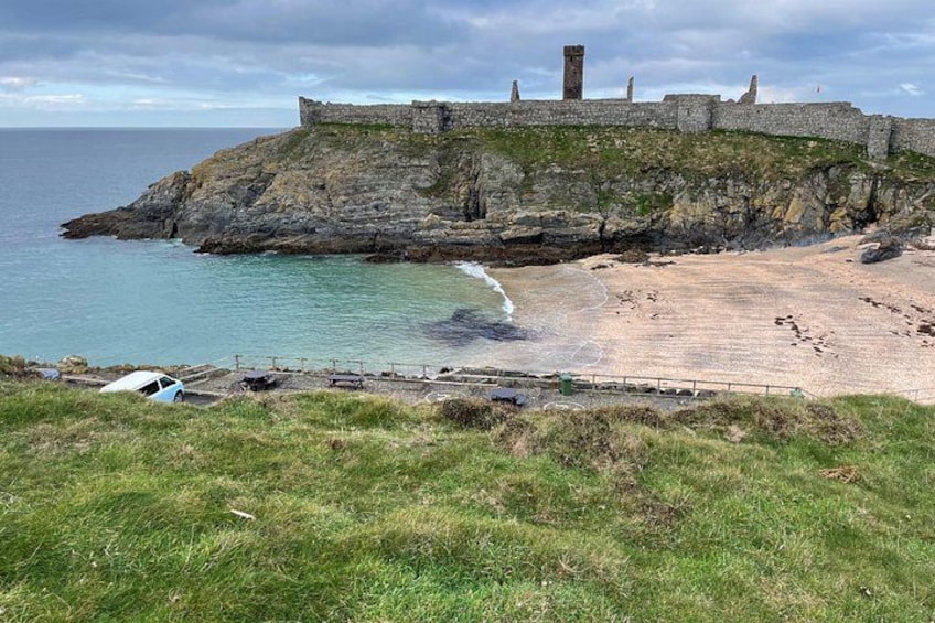 A coastal landscape with a grassy foreground, a sandy beach, and a stone fortification on a cliff. 1