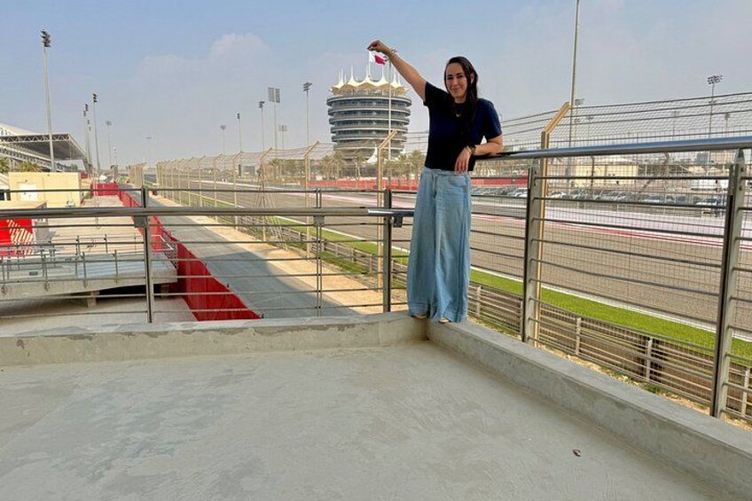 A person standing on a concrete platform with a railing, overlooking a racetrack and a stadium in the background. 5