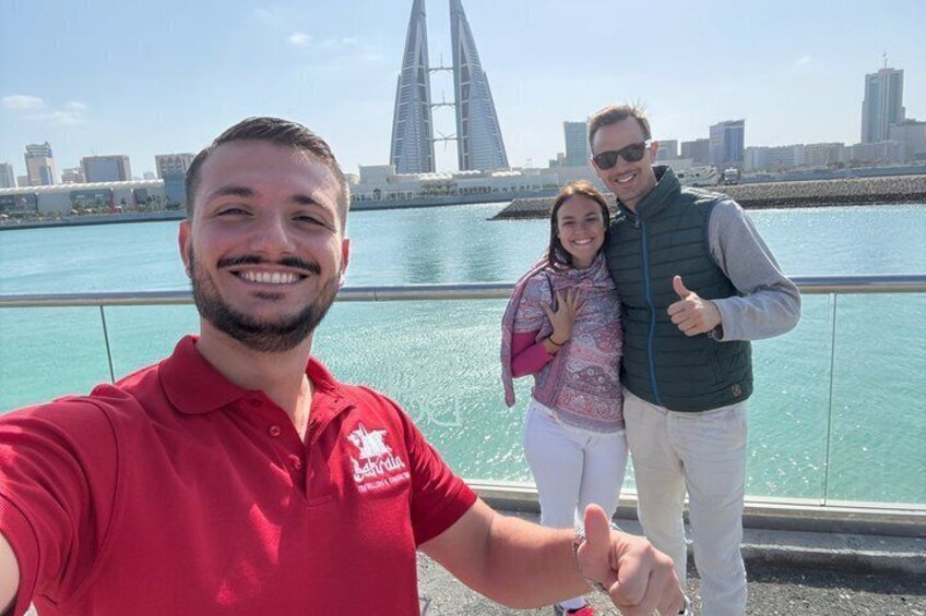 A person in a red shirt taking a selfie with a city skyline and a bridge in the background. 2