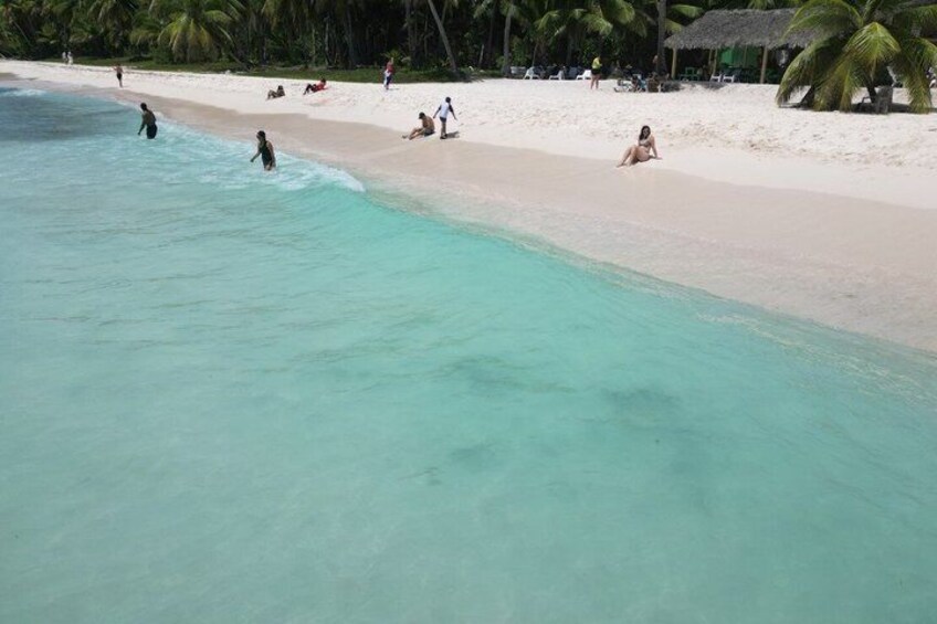 A beach with clear turquoise water, people swimming and sunbathing, and palm trees in the background. 5