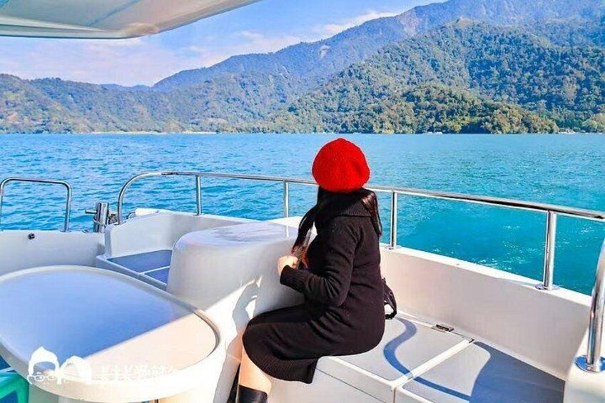 A person on a boat with a red beanie, water, and mountains in the background. 3