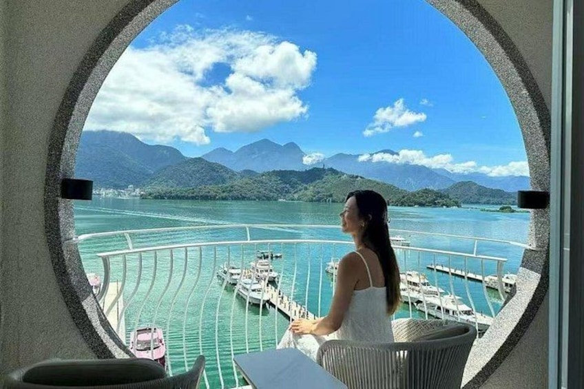 A woman on a balcony overlooking a marina with boats and a mountainous landscape. 4
