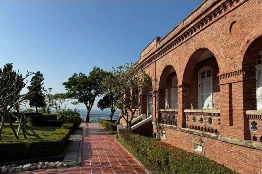 A brick building with arched windows and a paved pathway leading to a body of water. 4