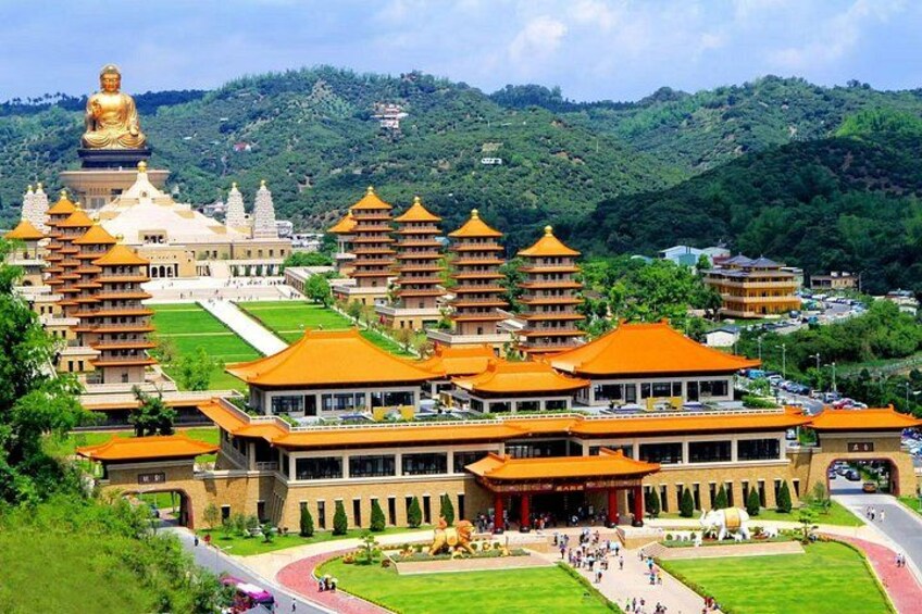 A large temple complex with multiple pagodas, a golden Buddha statue, and lush green hills in the background. 2