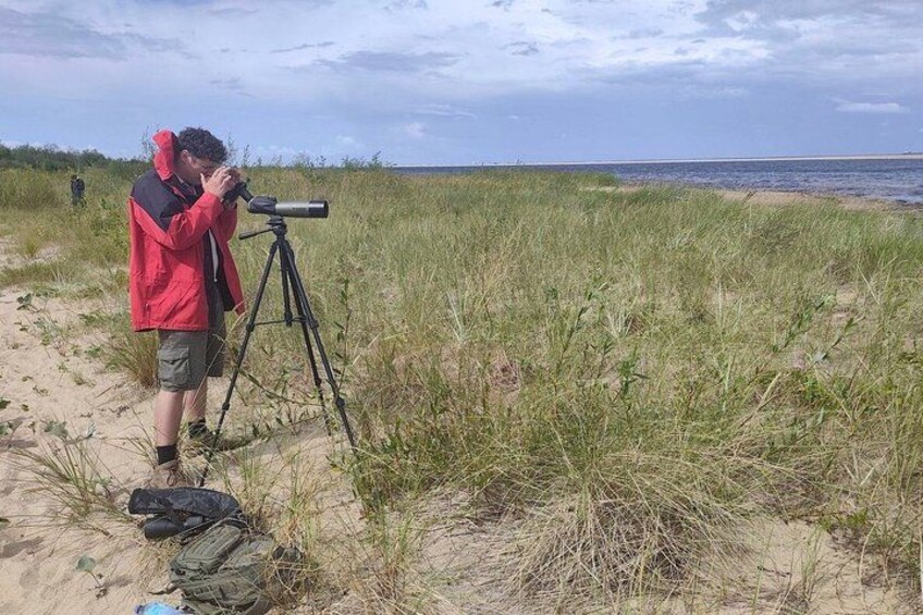 A person using a telescope on a beach with sand and grass. 2