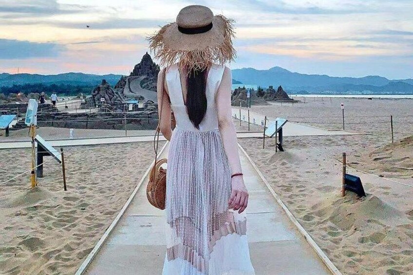 A person walking on a beach path, holding a straw hat and a bag. 3