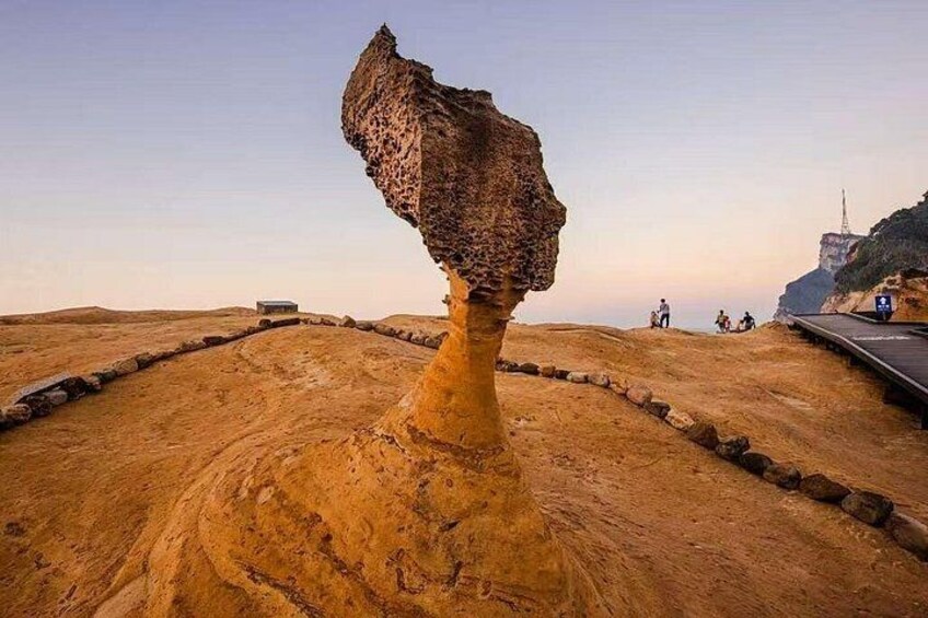 A large rock formation balanced on a pedestal, a paved path, and a distant tower. 2