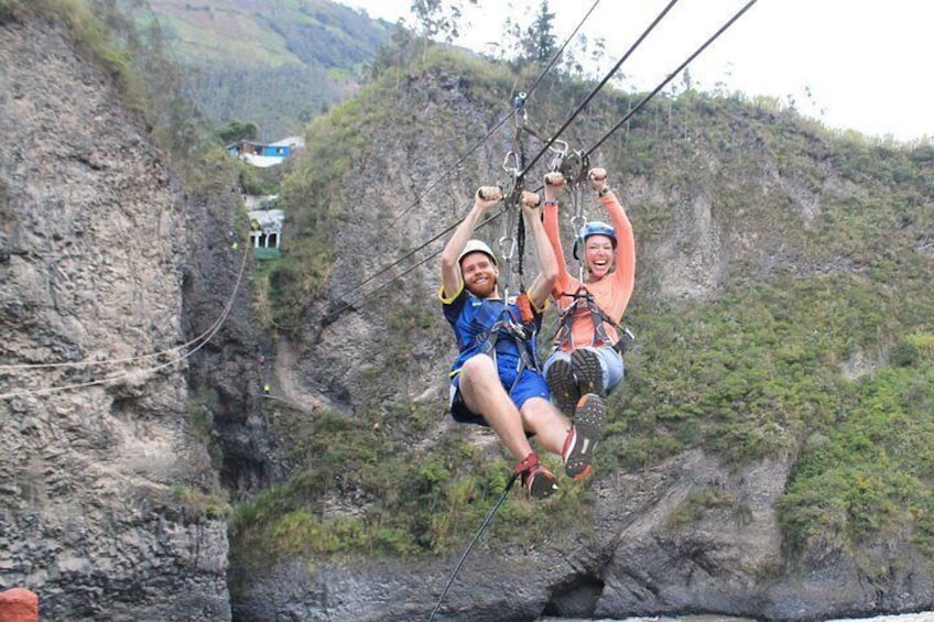 Two people zip-lining over a canyon with rocky cliffs and sparse vegetation. 3