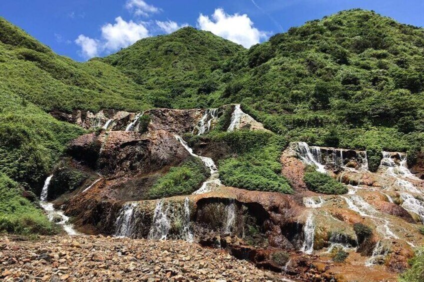 A series of waterfalls cascading down a rocky hillside surrounded by lush greenery. 4