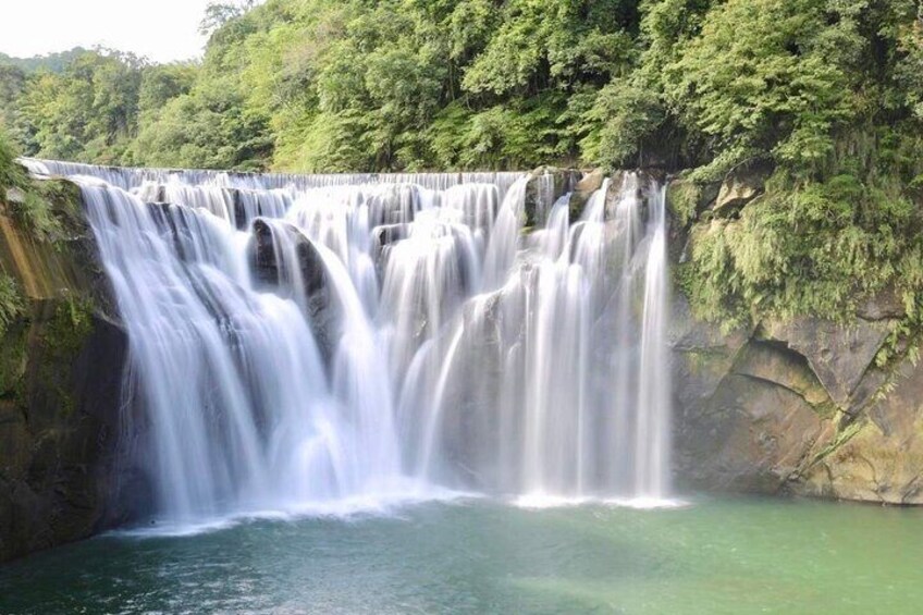 A multi-tiered waterfall cascading into a calm pool surrounded by lush greenery. 2