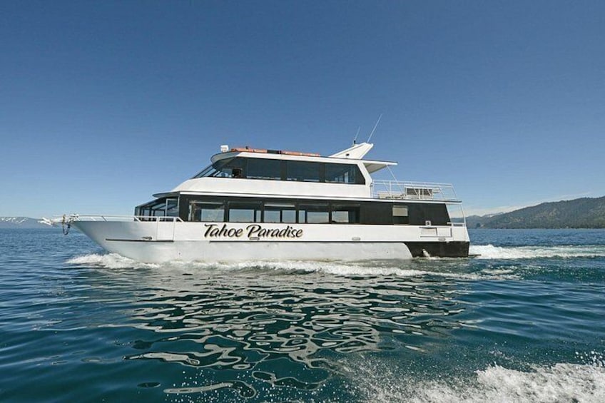 A white boat named Tahoe Paradise on a body of water with a clear sky. 2
