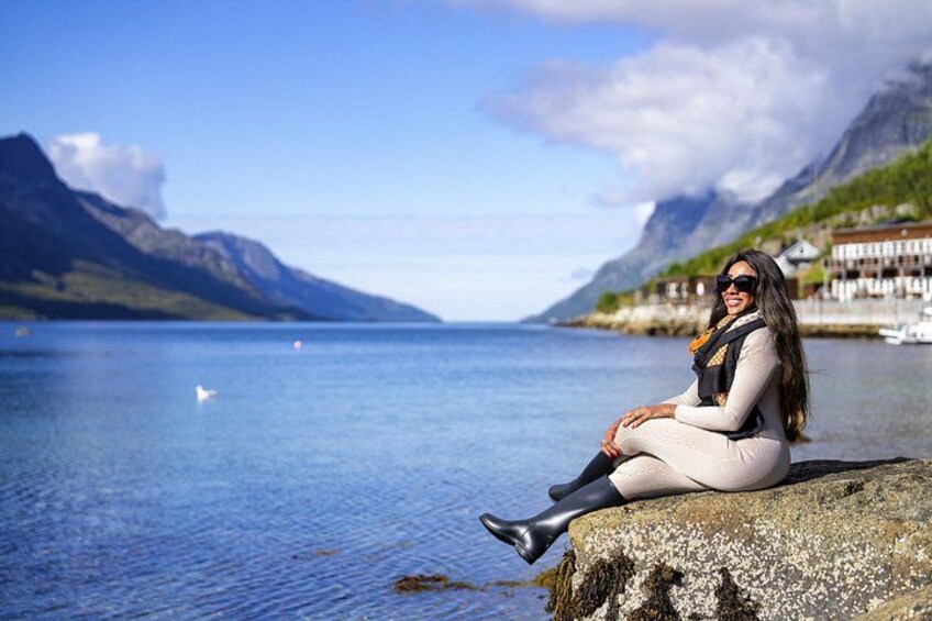 A person sitting on a rock by a lake with mountains in the background. 2