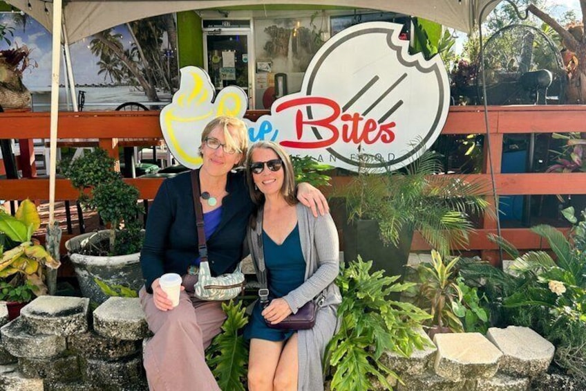 Two people sitting in front of a restaurant named 'Bites' with a large sign. 3