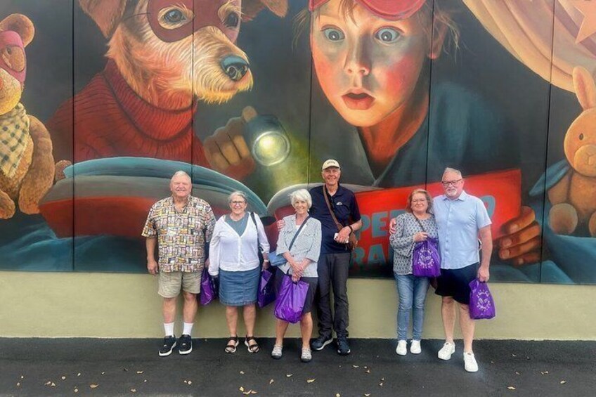 A group of people standing in front of a mural with a dog and a human figure. 2