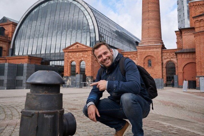 A person squatting next to a fire hydrant with a modern building and a brick tower in the background. 5