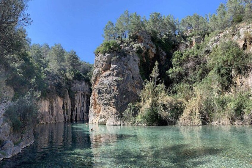 A clear river with rocky cliffs and dense vegetation. 5