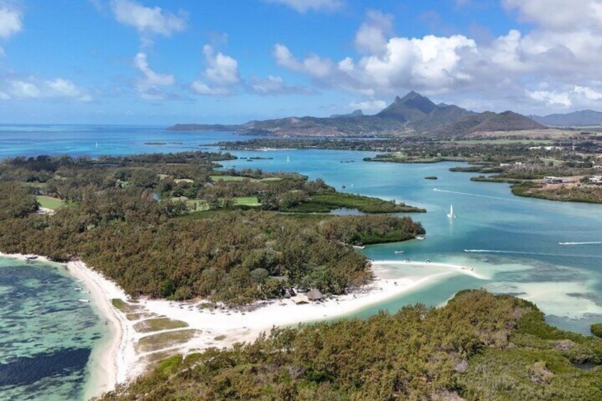 An aerial view of a coastal area with a beach, clear waters, and a distant mountain range. 5
