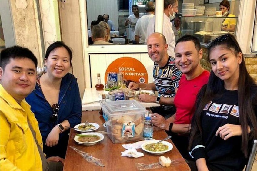 Un gruppo di persone sta cenando in un ristorante con un cartello che recita 'SOSYAL NOKTASI'. 1