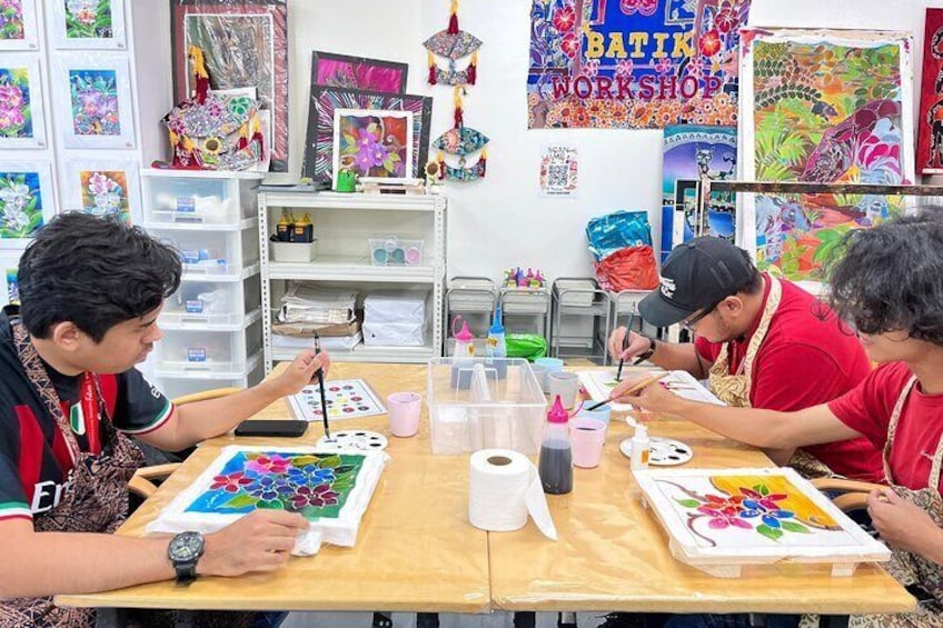 Drie personen schilderen aan een tafel in een werkplaats met kleurrijke kunstwerken op de muren. 5
