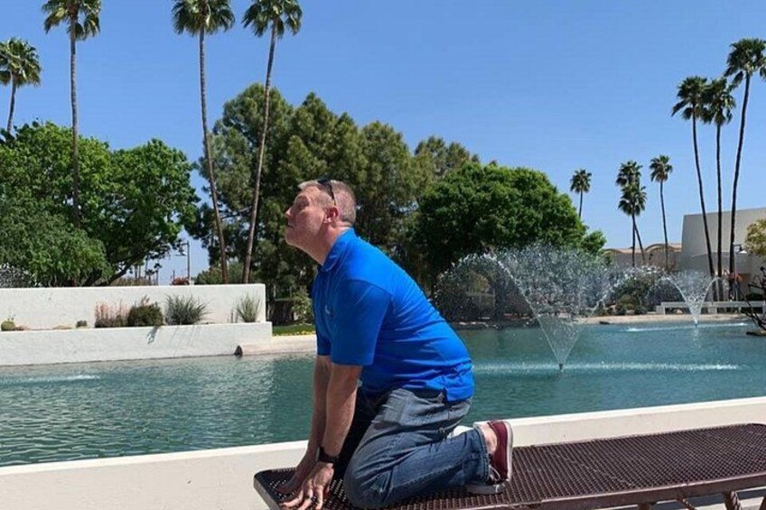 A person kneeling by a pool with palm trees and a fountain in the background. 2