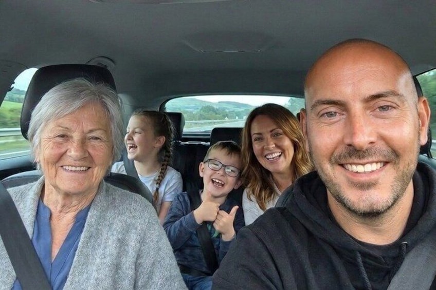 Four people in a car with a landscape of hills in the background. 2