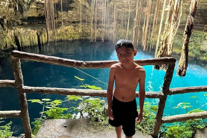 En person står på en träplattform med utsikt över en klar, blå pool omgiven av vegetation. 2