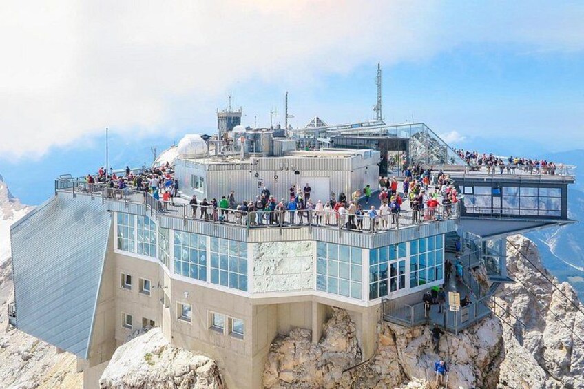 A glass observation deck with people on a mountain peak. 2