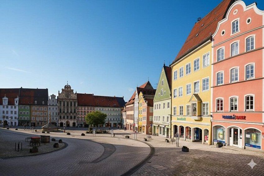 A cobblestone square with colorful historic buildings, a fountain, and a clear blue sky. 3
